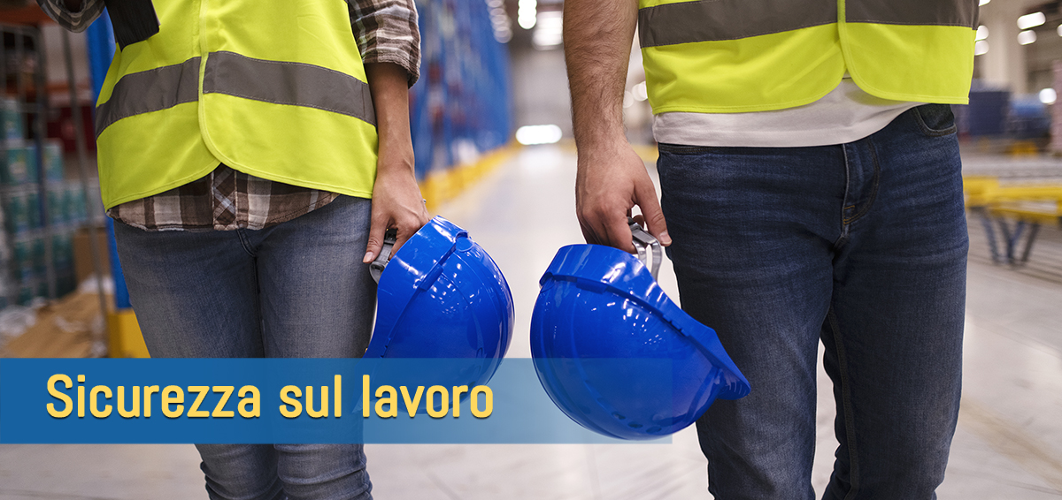 Two unrecognizable workers in reflective suit walking through warehouse and holding blue protective hardhats.